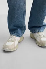 Zapatilla deportiva tipo running de color negro, perteneciente a la colección especial Origins. Presenta una parte superior confeccionada en una combinación de cuero con acabado de gamuza y tejido transpirable. Cuenta con una suela de volumen con diseño irregular y cierre mediante cordones.