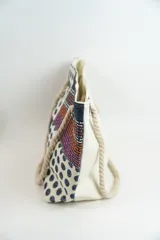 Bolso de playa o tote bag con diseño de patchwork en tonos rosados, naranjas y blancos. Presenta secciones con estampado de lunares rojos y secciones con tejido de rafia. Las asas son de cuerda trenzada.