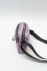 Cartera tipo bandolera de nylon color lila, con cierre frontal y correa ajustable negra.