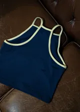 Musculosa deportiva de lycra color azul marino con ribetes y tirantes finos en color amarillo claro. Presenta un logo caligráfico en color amarillo claro en el pecho.