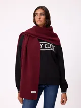 Bufanda de tejido de punto en color bordó, con textura acanalada y etiqueta de la marca Rusty en el extremo inferior.