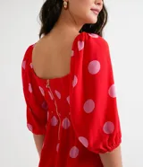 Vestido corto rojo con estampado de lunares rosas, escote cuadrado, mangas cortas abullonadas y volado en el ruedo.