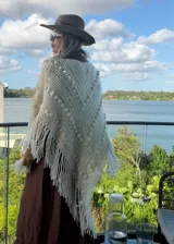 Ruana tejida artesanalmente en color crudo, con diseño triangular, textura de puntos en relieve y terminación con flecos largos en todo el borde.