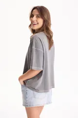 Remera de algodón gris con efecto lavado, corte semi boxy, mangas cortas y costuras en contraste. Presenta un pequeño bordado frontal con líneas curvas y la palabra "Ciao".