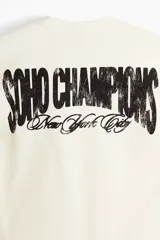 Remera de algodón en color blanco, de corte holgado, con cuello redondo acanalado, mangas cortas y hombros caídos. Presenta un pequeño estampado en el pecho con la inscripción "SOHO CHAMPIONS New York City".