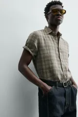 Camisa de lino color beige de corte relajado, con cuello solapa, manga corta y cierre frontal con botones.