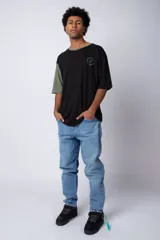 Remera de corte oversize en color beige, con cuello redondo en contraste negro y una manga en color negro. Presenta un pequeño estampado circular en el pecho con la frase 'Don't worry, be happy'.