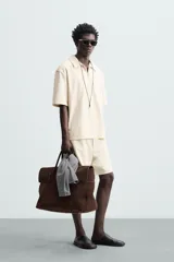 Bermuda de hombre color verde claro, de corte regular y tiro medio, con pinzas frontales, bolsillos laterales y bolsillos traseros de vivo. Cierre frontal con botón y cremallera.