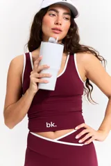 Conjunto deportivo compuesto por un top y un pantalón largo en color bordó. El top presenta un diseño con cuello redondo y ribetes blancos, con el logo 'bk.' estampado en el frente. El pantalón es de corte ajustado con cintura cruzada en V y detalle de ribete blanco, con terminación acampanada en los tobillos.