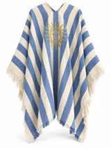 Ruana de playa con diseño de franjas verticales celestes y beige, adornada con un sol bordado en el pecho y flecos en los bordes.