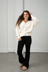 Saco de punto color blanco con cuello en V, cierre frontal con botones y apliques de flores bordadas en relieve. Presenta diseño de ochos y mangas largas con puños acanalados.