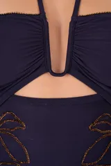 Traje de baño entero azul marino con escote bandeau, tirantes finos que se atan al cuello y bordado floral dorado en la parte inferior.