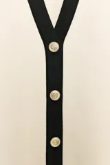 Chaqueta de punto color crudo con ribetes negros en el cuello en V, la botonera, el bajo y los puños de las mangas cortas. Cuenta con cierre frontal con botones dorados grabados.