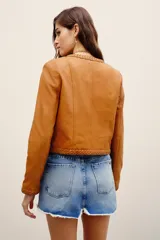 Saco corto de cuero ovino en color tostado, sin cuello, con detalles de trenzados en los bordes y bolsillos frontales con solapa.
