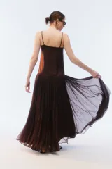 Vestido largo negro con breteles finos y escote recto, parte superior lisa y falda amplia de pliegues finos con gran movimiento y caída.
