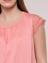 Remera blanca semi holgada de tejido suave, con escote redondo amplio, detalle de frunces en el centro del pecho y mangas cortas de crochet calado con bordes festoneados.