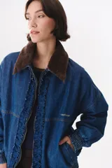 Campera de denim azul con corte oversized, cierre frontal y cuello de piel sintética marrón desmontable. Presenta detalles de volados en el frente, puños elásticos y logo bordado en el pecho.