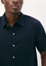 Camisa de manga corta con cuello clásico, cierre frontal de botones y bolsillo en el pecho. Presenta un corte entallado y un acabado de textura sutil.