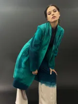 Tapado largo de lana merino color verde con teñido tie-dye en tonos oscuros. Tiene corte particular en los hombros y bolsillos laterales.