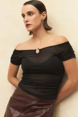 Top negro de tejido semitransparente con diseño de hombros descubiertos, mangas cortas y detalle de aplique metálico en el escote.