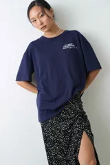 Remera de algodón gris melange con corte oversize, manga corta y estampa localizada en el frente con motivos deportivos en tonos verde y rosado.
