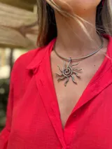 Collar tipo choker con base rígida plateada y dije colgante de sol estilizado con espirales y rayos, hecho a mano en alambre.