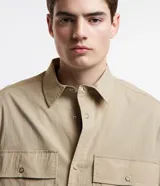Camisa overshirt color beige, de corte recto, con cuello solapa, abotonadura frontal, mangas largas y dos bolsillos de parche con solapa en el pecho.