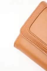 Billetera compacta de cuero sintético negro, con solapa que combina texturas lisas y efecto reptil. Incluye un aplique metálico circular con logo grabado en el frente y cierre con broche.