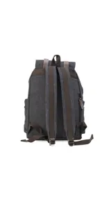 Mochila de tela canvas color verde oliva con tapa y detalles en cuero sintético marrón. Cuenta con cierre superior tipo marinero, múltiples bolsillos externos con cierre y correas ajustables.