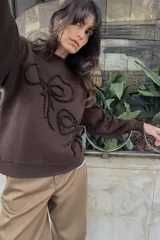 Sudadera marrón de cuello redondo y manga larga, con detalle de lazos en relieve en el delantero y acabados en rib a tono.