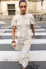 Blusa de manga corta abullonada con diseño a cuadros, cuello con volante y acabados elásticos. Cuenta con aberturas y lazos ajustables en los laterales.