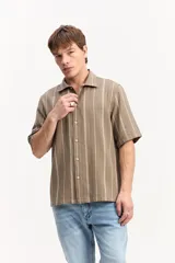 Camisa de manga corta oversize en tejido rústico, con diseño de rayas verticales celestes y blancas, cuello clásico y cierre frontal de botones.