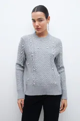 Sweater color beige melange de tejido de punto con diseño de trenzas y detalles de perlas en el frente y las mangas.
