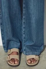 Sandalia plana color beige de serraje, con dos tiras anchas en el empeine ajustables con hebillas doradas y suela plana.