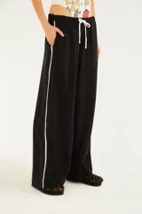 Pantalón negro de silueta amplia y caída relajada, con cintura elástica ajustable mediante cordón blanco y detalles de vivos laterales en color blanco.