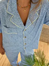 Pijama de dos piezas, compuesto por una camisa de manga corta con cuello y ribetes en color azul marino, y pantalón largo. El conjunto presenta un estampado floral pequeño en tonos arena y marrón.