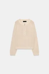 Sweater de punto color beige con cuello redondo, manga larga y cierre frontal parcial con botones. Presenta terminaciones en rib en cuello, puños y dobladillo.