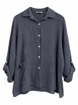 Camisa azul marino de lino con cuello camisero, cierre frontal de botones claros, mangas largas con trabilla para sujetar arremangadas y bolsillos frontales aplicados.