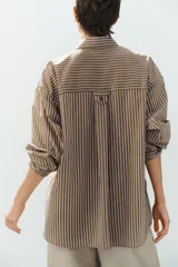 Camisa de popelina a rayas marrones, blancas y celestes, con cuello clásico, manga larga, bolsillo frontal de parche y cierre de botones.