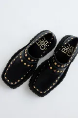 Mocasines de cuero color marrón con suela track negra y tachas doradas.