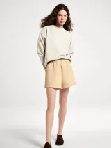 Buzo de cuello redondo en color beige, con diseño liso, mangas largas y puños y ruedo acanalados.