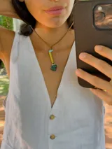 Collar con tiento de cuero marrón y dije con forma irregular, compuesto por un cilindro de metal dorado, una piedra amatista y una piedra de cuarzo transparente.