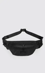 Riñonera negra confeccionada en cordura impermeable de alta resistencia. Presenta tres compartimentos principales con cierres metálicos, un bolsillo lateral adicional y una correa ajustable de alta densidad con broche de seguridad. Incluye una chapa metálica decorativa en el frente.