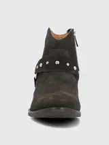 Bota corta de mujer color gris oscuro o marrón oscuro, estilo botín biker, confeccionada en gamuza. Presenta una tira decorativa con tachas metálicas plateadas y hebilla. Tiene un taco bajo y punta ligeramente afilada.