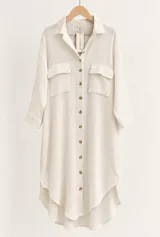 Vestido camisero largo de lino color beige, con cuello clásico, mangas largas, bolsillos frontales con solapa y cierre de botones marrones.