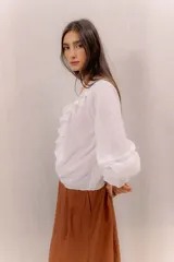 Camisa blanca de algodón con escote en V, volados delanteros con detalles de encaje y mangas largas con puños fruncidos.