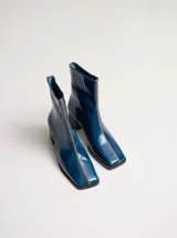 Botas de caña media color marrón, confeccionadas en cuero con acabado brillante. Presentan punta cuadrada, taco de madera y un distintivo bordado decorativo en color rojo que recorre el empeine hasta la punta.