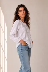 Blusa blanca de manga larga con detalles bordados en el frente y cuello redondo con cierre parcial de botones.