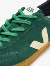 Championes Veja modelo Volley, confeccionados en gamuza color verde con detalles en crema. Presentan el logo lateral en forma de V, suela de goma color caramelo y cierre mediante cordones.
