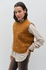 Chaleco de punto color celeste, con diseño de trenzas y pequeñas flores bordadas a mano en color marrón oscuro. Presenta cuello redondo y terminaciones acanaladas.